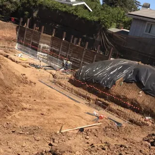 A shored excavation on a sloped lot, with rebar and plastic sheeting